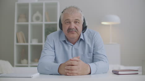middle-aged-man-with-headphones-on-head-is-nodding-and-looking-at-camera-video-calling-and-online-chatting-concept